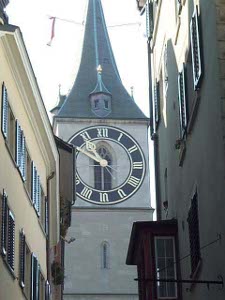 Taken with a telephoto lens, the clock appears on a large green-roofed church tower framed by buildings in the foreground