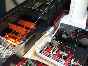 Two vessels, one steam with a bright red paddlewheel, one with polished steel crankshaft, all colored white and black and red, on display
