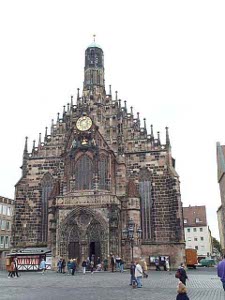 Lots of little towers atop the old red stone church, with a clock near the top, and a bell tower above.