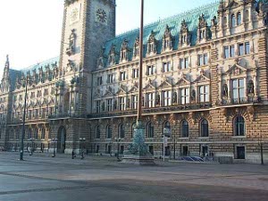 The enormous five-story city hall with a huge tower is constructed out of light and dark tan stone with a greenish steep roof