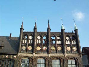 This part of the town hall features a segment of wall topped by five columns with conical tops, all painted brown, with round windows over arches, decorated with white civic designs