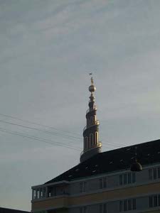 A blue and gold tower spirals up to a point atop which is a golden ball and a weather vane