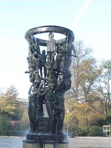 The bronze fountain stands perhaps 15 feet high, with a ring at the top from which water descends in a dripping rush, cascading over many bronze figures standing atop one another