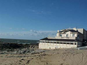 The restaurant and guest house is white, with a row of windows overlooking the sandy beach and the ocean
