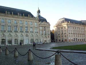 Large four-story public buildings in light tan stone fronting a square surrounded by chain strung between bollards