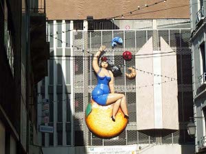 The sculpture is a lady in a low cut short blue dress sitting on top of the world with symbols for food in the air above her.