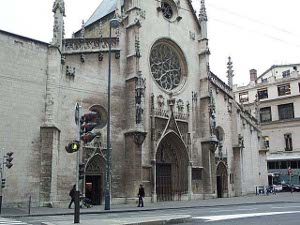 The plaque says there was a church here starting in the 13th century; this building was begun in the 14th.  It is a light tan stone, with a center rose window and tower.