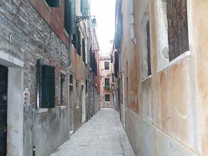 The street is perhaps 8 feet wide, with no curbs, sidewalks, just the sides of the buildings, which are plain, undecorated stucco and brick, with plain windows
