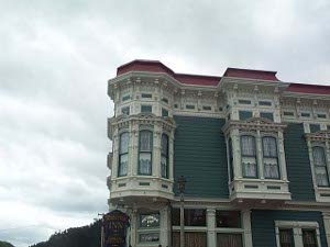 A green frame building with a red roof, this Victorian building has elaborate cream trim and bay windows that jut out over the street