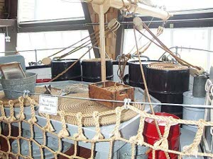 The deck hsa oil drums, coils of line, a washboard and bucket, spars, riggin, and ropework