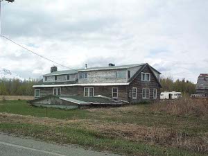 The old homestead is buried except for the roof; the newer farmhouse is in the rear.  Both are weathered gray board
