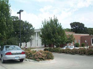 Partly hidden behind trees, the red bick library has a wide porch painted white in front