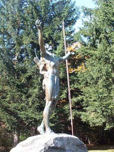 The Indian, sculpted in bronze, looking more like a greek god, stands atop a large boulder with his hands reaching towards the heavens