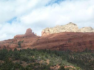 beyond a shrubby hill in the foreground, there is a salmon-colored sandy mountain behind which is a white rock butte