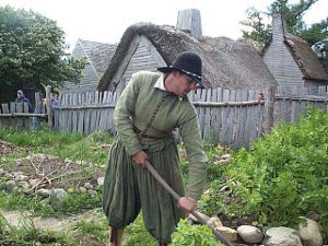 Wearing a broad-brimmed black hat and loose fitting green clothes, Governor Bradford is hoeing his garden