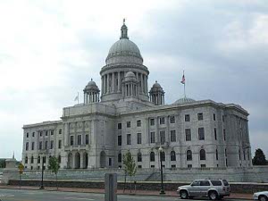 A four-story grey stone building is topped by a dome of equal height, with a green roof; two smaller columned domes are front and back of the main dome.