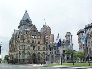 A six story Richardsonian building in two shades of brown stone dominates the corner across from a park.