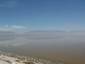 The lake is glassy smooth, so in the distance the reflection of mountains is perfect.  The sky is blue, but a brownish haze colors the lake.