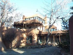 Three stories tall in tan stucco, with a windowed room on the top floor, the Luhan House is shaded by trees.