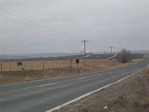 The photo is taken perhaps half a mile from the feedlot, and in the distance the dark lots full of cattle stretch from one side of the photo to the other.