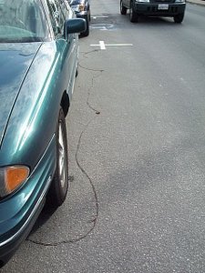 The dark colored yarn snakes down the asphalt pavement of the street, going beneath cars