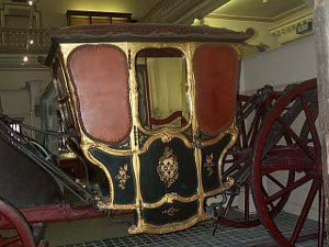 A black carriage with gold trim and four large red and black wheels