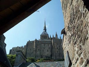 Long stairs can be seen ascending towards the abbey, with the spire piercing the blue sky.
