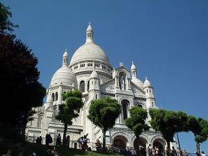 Looking up a row of neatly trimmed trees masks part of the magnificent church of Sacre Coeur, built of white marble and topped by an immence and graceful dome, with matching domes on the smaller towers.