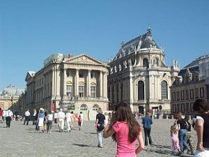 People walk across a huge cobblestone courtyard to the entrance to the imposing chateau of Versailles