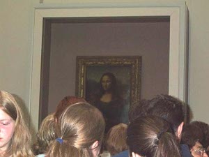 The Mona Lisa is behind tinted glass, and dozens of heads are crowded in front to get a glimpse of the painting