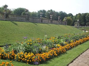 At the base of a grassy bank is a long bed of flowers next to a dirt walking path
