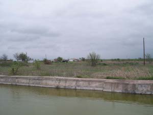 Water fills the remains of a dairy shed, with unused grassy fields and a mobile home in the bleak background at the forme Branch Davidian Complex near Waco, Texas.
