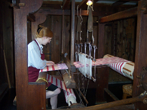 A weaver sits in the frame of a large wooden loom