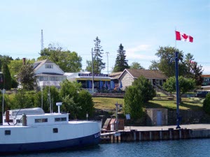 A dock, a flag, and a grassy hill front the main street of downtown Tobermory