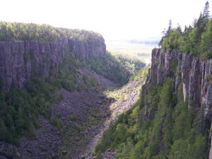 The stone-walled canyon in the near view stretches out to flat lake and forest in the distance