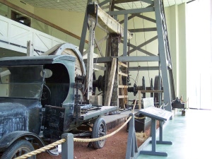 An old pickup truck is hooked up to provide motive power to an early Texas oil pump with the drilling rig standing above