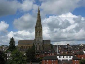 The church dominates the surrounding neighborhood, and the steeple rises over the nave, in a cathedral shape, to reach the sky covered with cumulus clouds.