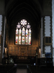 The stained glass window is surrounded with wood; dark pews are in the foreground.