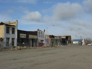 A wide dirt street fronted by old brick buildings damaged by the earthquake