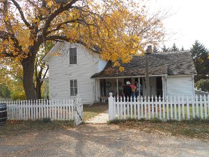 The white two-story house is surrounded by a picket fence.