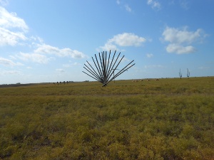 A large sculpture shows black metal beams sticking up from the ground in a fan shape; the buried cars are all but invisible.