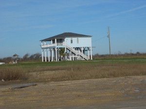 A white frame house has been built high supported by 25 vertical beams about 15 feet above ground level