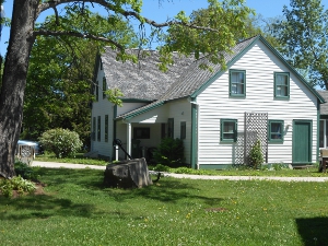 A white frame house with green windows and doors and a gray roof, surrounded by trees1