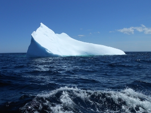 The iceberg is triangular in shape (above the water) and makes a stark contrast to the surrounding water.