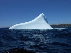 The iceberg is triangular in shape (above the water) and makes a stark contrast to the surrounding water.