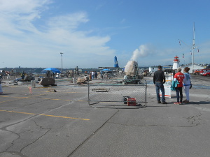 A huge concrete yard is surrounded by a safety fence and visitors watch sculptors working on their projects