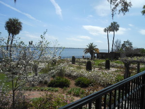 White dogwood and azalea flowers along with palm trees and lovely landscaping, define the garden against the background of the Saint Johns River and a light blue sky with puffy clouds.