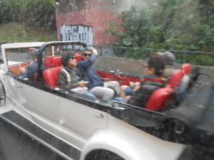 The silver white limo has red upholstery and four persons sit in the open back compartment with the tour driver ahead.