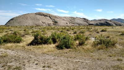 The huge grey stone monolith rises up from the surrounding flat dry plain dotted with small green scrub.