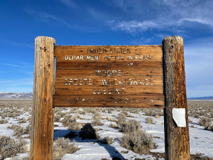 The large sign consists of planks of brown wood supported by two large wooden poles, with the letters burned into the sign and then painted white.